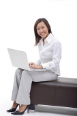 Business woman sitting on bench with laptop, smiling at camera - Asia Images Group
