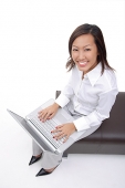 Woman sitting on bench with laptop, smiling at camera - Asia Images Group