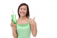 Young woman holding bottled drink, making thumbs up sign - Asia Images Group