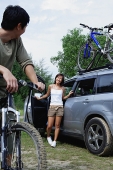 Man on a bike turning to look at woman standing next to car - Asia Images Group
