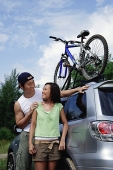 Couple standing next to SUV, looking at each other - Asia Images Group