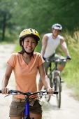 Couple cycling, woman in foreground, looking at camera - Asia Images Group