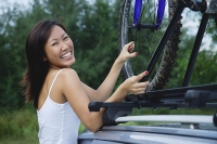 Woman securing bike on top of car, smiling at camera - Asia Images Group
