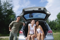 Women sitting in boot of car, man leaning on car - Asia Images Group
