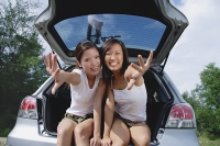Young women sitting in boot of car, reaching towards camera - Asia Images Group