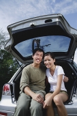 Couple sitting in boot of car, smiling at camera - Asia Images Group