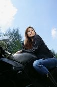 Young woman sitting on motorcycle, looking away, low angle view - Asia Images Group