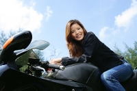 Young woman sitting on motorcycle, smiling at camera, low angle view - Asia Images Group