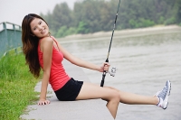 Woman sitting by river, holding fishing rod - Asia Images Group