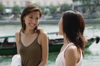 Two women smiling at each other, river behind them - Asia Images Group