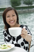 Young woman holding cappuccino cup, towards camera - Asia Images Group
