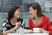 Two women at sidewalk cafe having lunch, smiling at each other - Asia Images Group