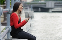 Woman sitting by river, listening to MP3 player - Asia Images Group