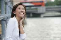 Woman sitting by river, smiling, looking up - Asia Images Group