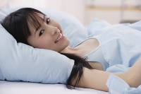 Young woman lying on bed, smiling at camera - Asia Images Group