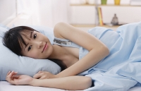 Young woman lying on bed, smiling - Asia Images Group