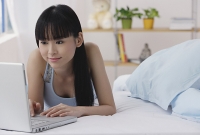 Young woman lying on bed, using laptop - Asia Images Group