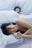 Young woman lying on bed, looking at mobile phone - Asia Images Group