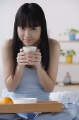 Young woman sitting on bed, holding cup of coffee - Asia Images Group