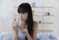 Young woman holding glass of water and pills, looking away - Asia Images Group