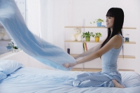 Young woman holding blanket, making the bed - Asia Images Group