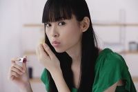 Young woman applying nail polish, blowing on nails - Asia Images Group
