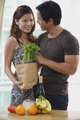 Couple smiling at each other, woman holding shopping bag with groceries - Asia Images Group