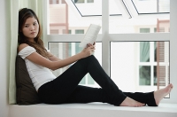 Woman sitting on bay window holding a book - Asia Images Group