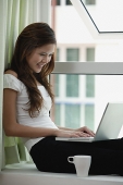 Woman sitting by window using a laptop - Asia Images Group