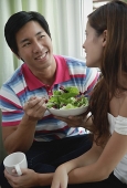 Couple talking, man eating a salad, woman holding a mug - Asia Images Group