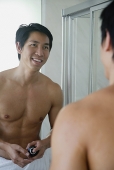 Man in bathroom, looking at mirror - Asia Images Group