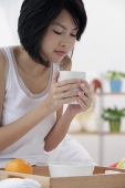 Young woman having breakfast, holding coffee mug - Asia Images Group