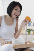 Young woman having breakfast in bed, holding orange, smiling - Asia Images Group