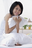 Young woman sitting on bed, hugging pillow, smiling - Asia Images Group