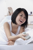 Young woman with TV remote control, smiling - Asia Images Group