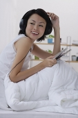 Young woman sitting on bed, listening to music - Asia Images Group