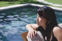 Young woman leaning on deck chair by swimming pool - Asia Images Group