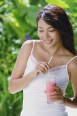 Young woman holding drink, smiling, looking away - Asia Images Group