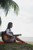 Young woman sitting on beach playing a guitar - Asia Images Group