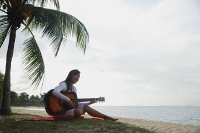 Young woman sitting on beach with a guitar - Asia Images Group