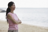 Woman standing on beach, arms crossed, looking away - Asia Images Group