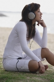 Young woman sitting on beach, listening to music, hand on chin - Asia Images Group