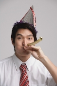 Businessman wearing party hat and using noisemaker - Asia Images Group