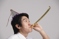 Man wearing party hat and using noisemaker - Asia Images Group