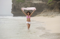 Woman in pink bikini, running along beach, holding scarf in air - Asia Images Group