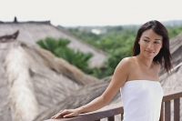 Young woman leaning on railing looking away, thatched roofs behind her - Asia Images Group