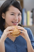 Young woman eating a burger, smiling - Asia Images Group