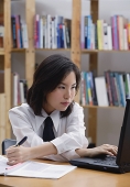 Young woman in library, using laptop and writing - Asia Images Group