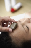 Young woman in spa, massage stone being placed on her forehead - Asia Images Group