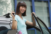 Young woman getting into car, smiling at camera - Asia Images Group